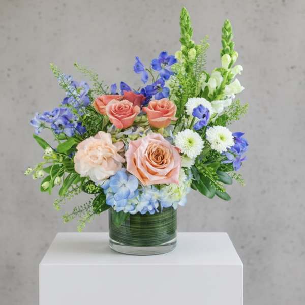 Mixed bouquet of roses, blue flowers, and white daisies in a glass vase