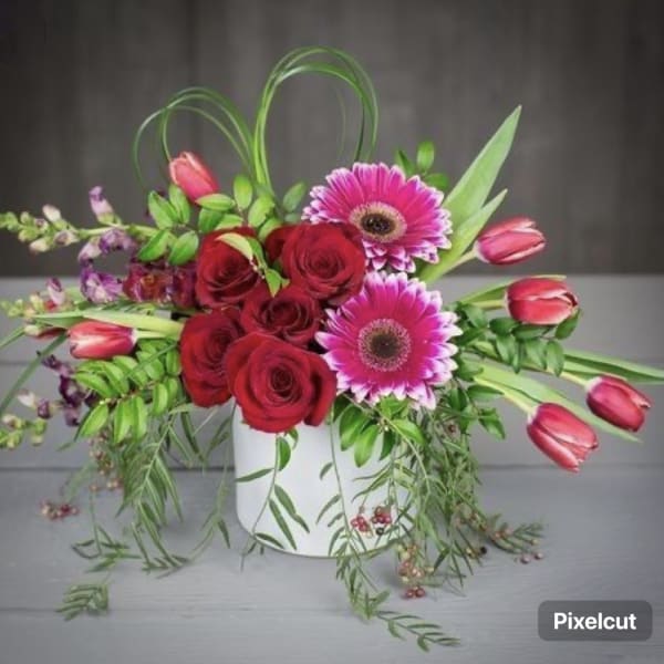 Red roses and pink gerbera daisies in a white vase with trailing greenery