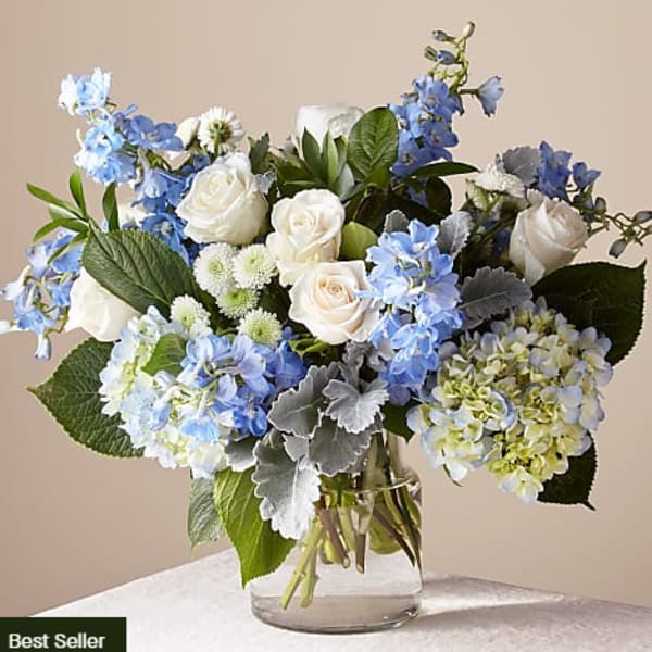 Arrangement of white roses, blue hydrangeas and blue delphinium in a clear glass vase