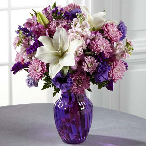 Purple and pink mixed bouquet with white lilies in a purple glass vase