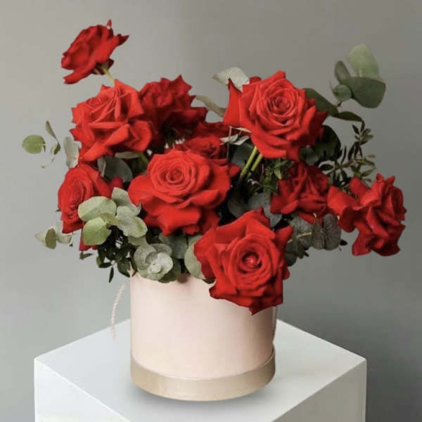 Red roses arranged in a pale round box with eucalyptus