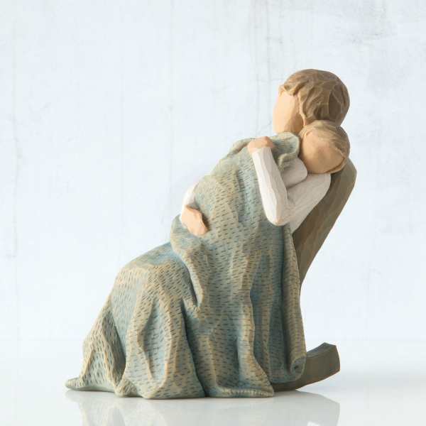 Wooden figurine of an adult holding a child wrapped in a blanket