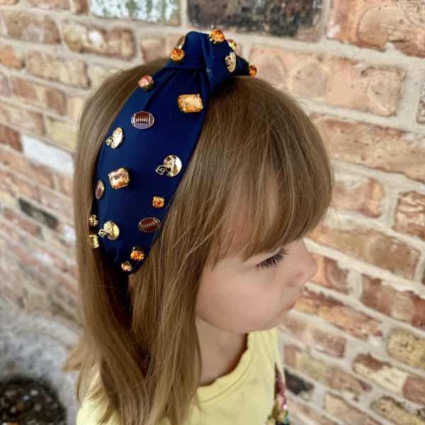 Child wearing a navy jeweled headband against a brick wall