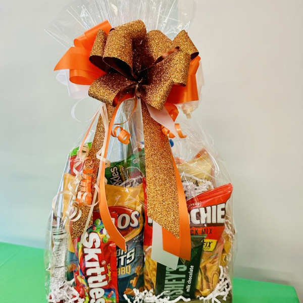 Snack gift basket wrapped in cellophane with a large glittery orange bow and assorted chips and candy.