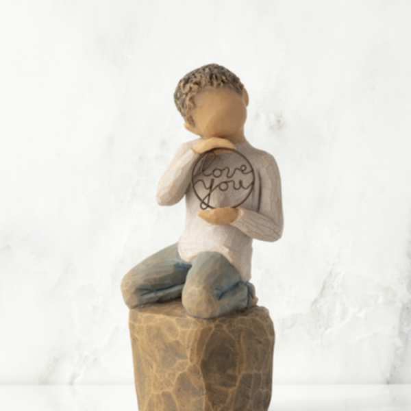 Small figurine of a seated child holding a heart-shaped sign that says love you