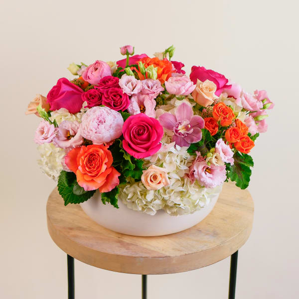 Mixed pink and orange flower arrangement in a white bowl vase