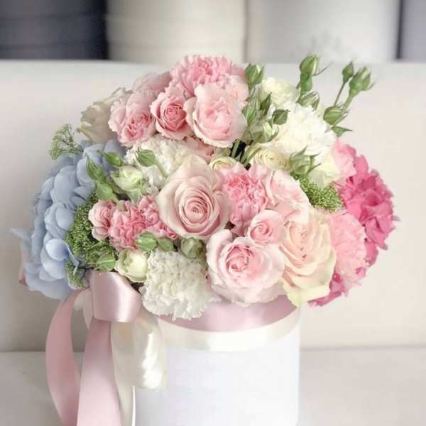 Pastel bouquet of roses, hydrangeas, and carnations in a white hat box with pink ribbon