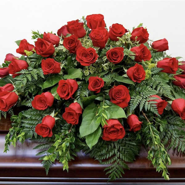 Red rose casket spray with mixed greenery on a wooden casket