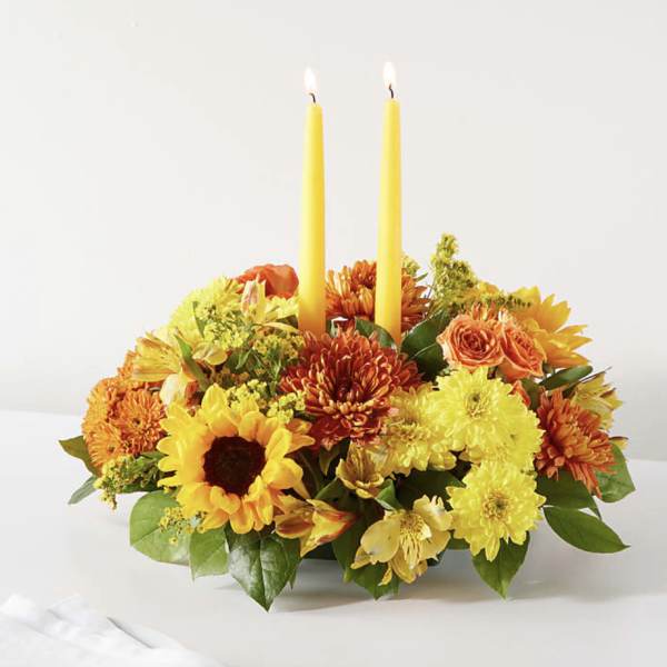 Yellow and orange floral centerpiece with two lit taper candles
