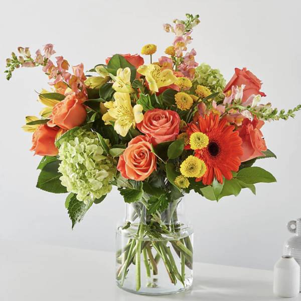 Bouquet of orange roses, yellow lilies, and gerbera daisies in a glass vase