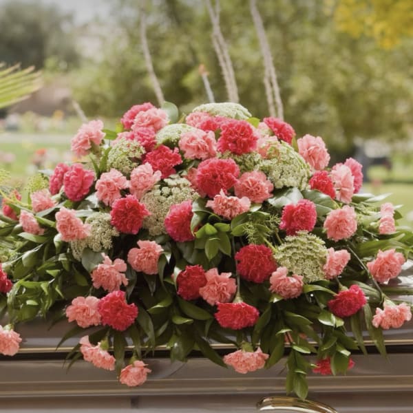 Pink and red carnations arranged on a casket with greenery