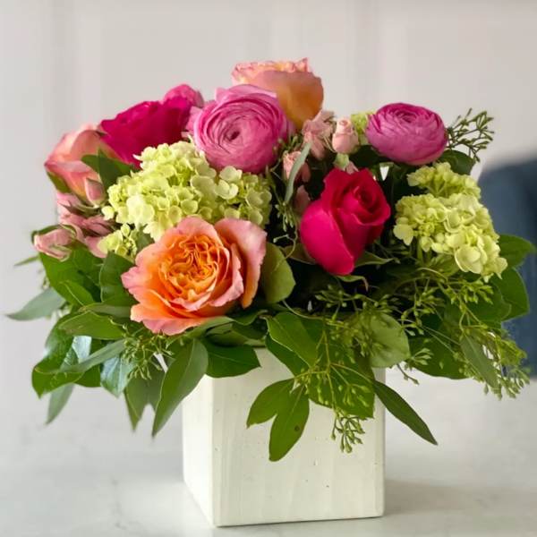 Pink and orange roses with pale green hydrangeas in a white vase