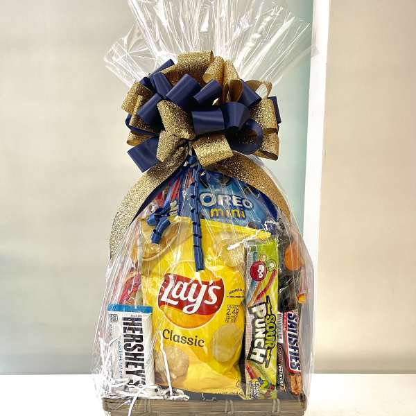 Gift basket of assorted snacks wrapped in cellophane with a large navy and gold bow