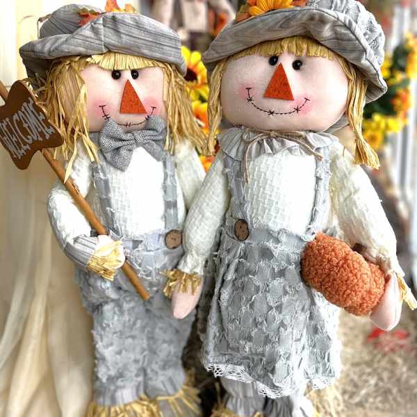 Two scarecrow dolls in gray outfits, one holding a sign and the other a pumpkin
