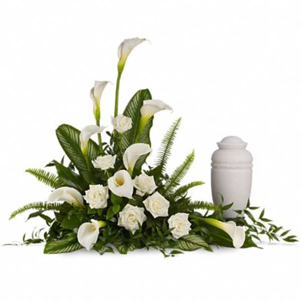 White calla lily and rose sympathy arrangement beside a white cremation urn.