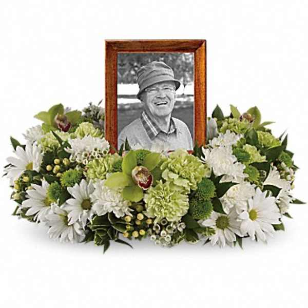Low white and green floral wreath encircling a wooden photo frame with a portrait.