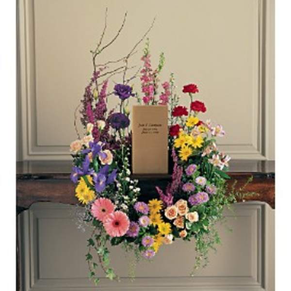 Colorful mixed flower wreath with central memorial card displayed on a wooden surface
