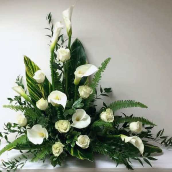 White calla lilies and roses arranged with large glossy leaves in a low, fan-shaped display