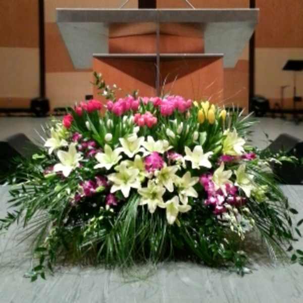 Large stage arrangement of white lilies and pink and yellow tulips set in front of a podium