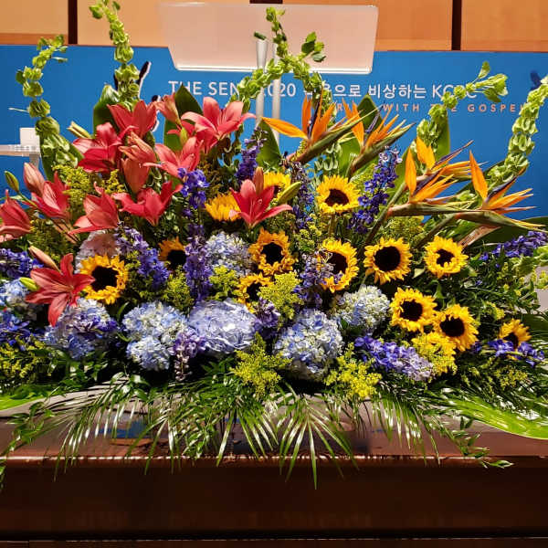 Large stage arrangement with yellow sunflowers, pink lilies, blue hydrangeas and orange tropical flowers.