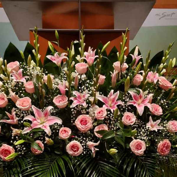 Large low arrangement of pink roses, pink lilies, and white filler flowers in front of a stage.