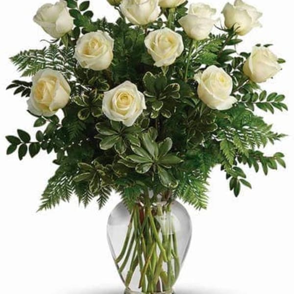 White roses arranged in a clear glass vase with lush greenery