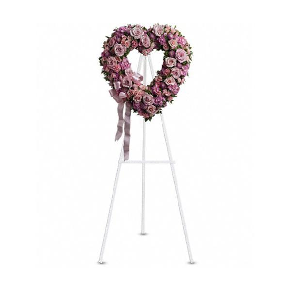 Heart-shaped wreath of pink and lavender roses on a white easel with ribbon.
