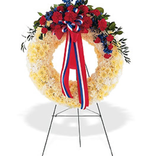 Patriotic wreath of yellow flowers with red and blue accents on a metal easel