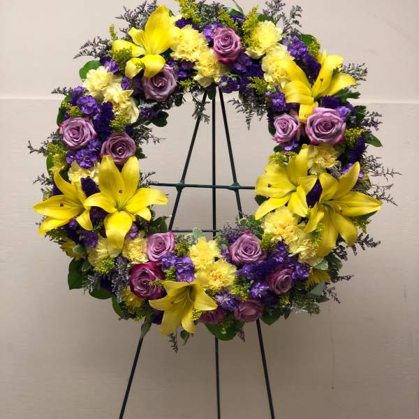 Standing wreath of yellow lilies, pale yellow blooms, and lavender and purple flowers on an easel