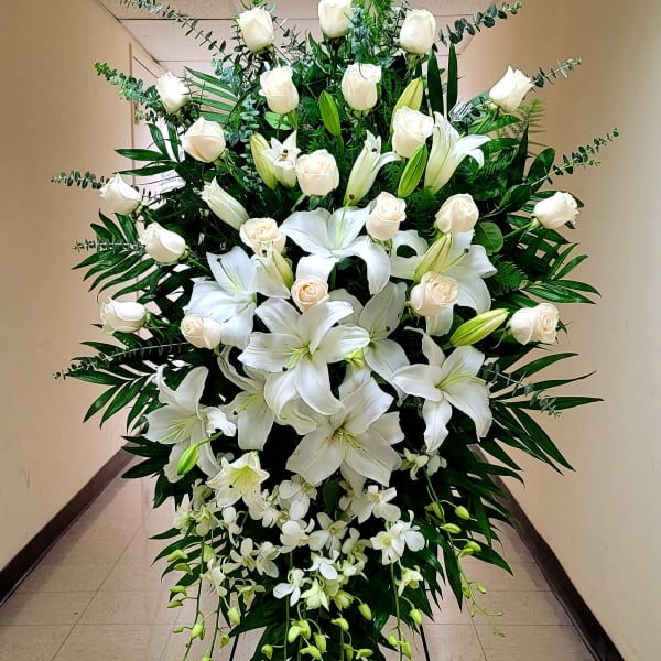 Tall standing spray of white roses, lilies, and orchids on an easel.