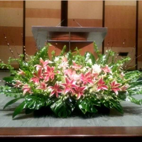 Large low arrangement of pink lilies and lush foliage in front of a podium on a stage