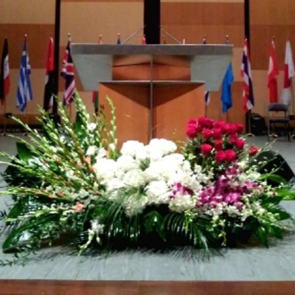 Large stage floral spray with white blooms, red roses, and purple orchids arranged in front of a podium