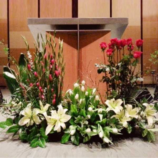 Large altar floral arrangement with white lilies, tulips, and red roses in front of a podium