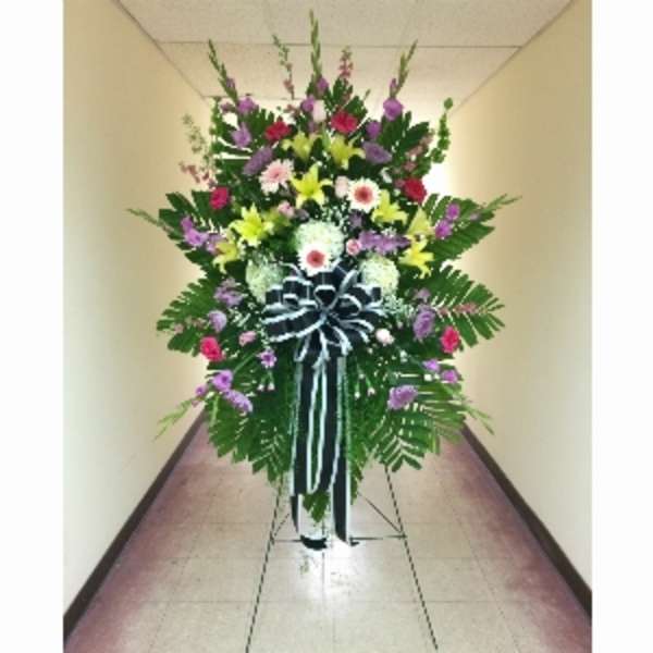 Tall standing spray of mixed colorful flowers with a large black and white bow on an easel.