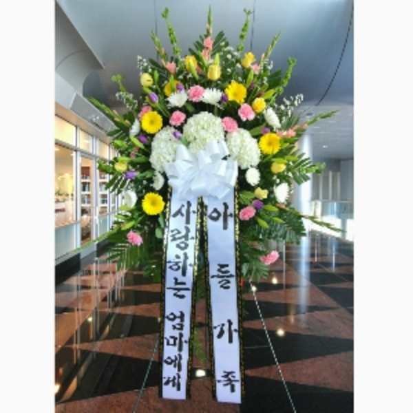 Tall standing sympathy spray with yellow, pink, and white flowers and Korean message ribbons on an easel