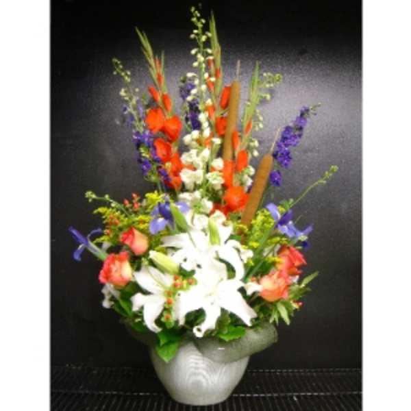 Tall mixed arrangement with white lilies and bright orange and purple flowers in a light gray urn-style vase