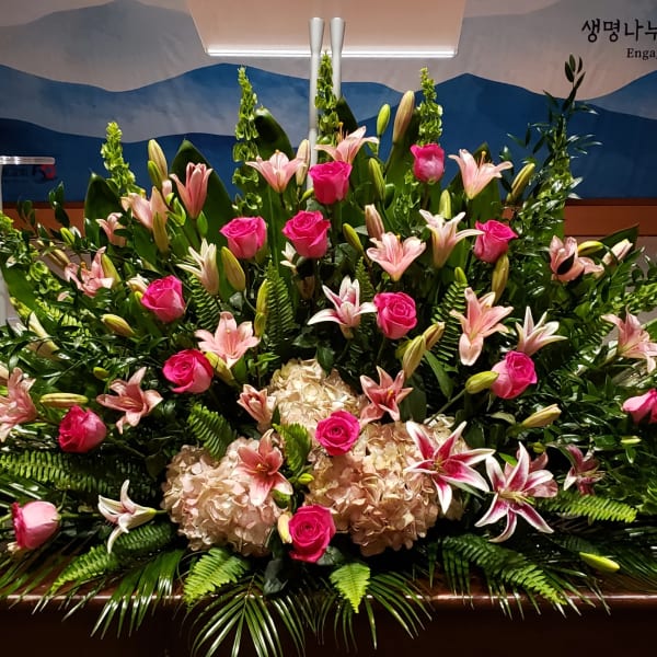 Large fan-shaped arrangement of pink roses, lilies, and hydrangeas on a stage backdrop