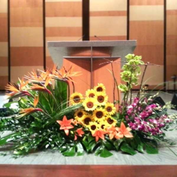 Large stage arrangement with birds of paradise, sunflowers, lilies, and orchids in front of a podium