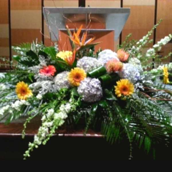 Large low centerpiece of hydrangeas, gerbera daisies, and a tropical bloom in front of a podium