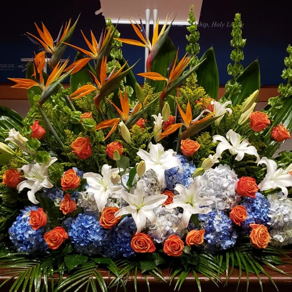 Large altar-style arrangement with orange, blue, and white flowers including lilies and hydrangeas