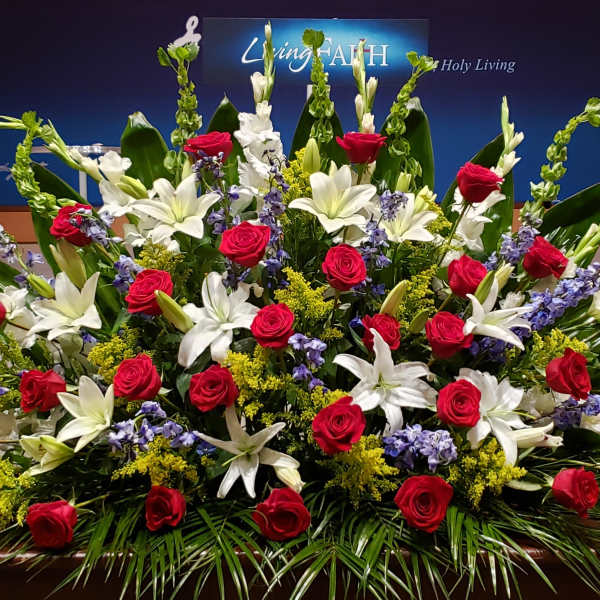 Large altar arrangement of red roses, white lilies, and blue flowers in a fan shape on a stage