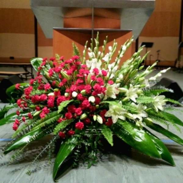 Large red carnation and white lily stage arrangement with abundant foliage in front of a podium