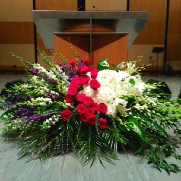Large red, white, and purple floral spray with roses and lilies arranged in front of a podium.