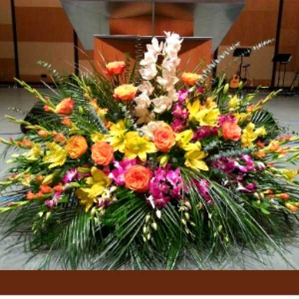 Large stage arrangement with yellow lilies, orange roses, and pink orchids in a fan-shaped design