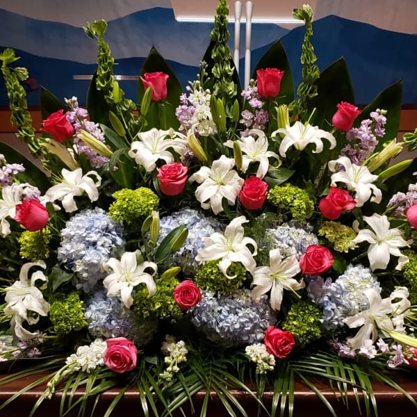 Large altar arrangement with white lilies, pink roses, blue hydrangeas, and green accents