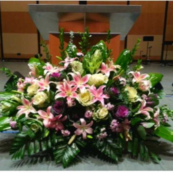 Large mixed arrangement of pink lilies and cream blooms displayed in front of a podium.