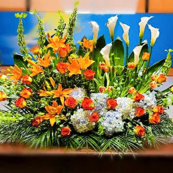 Large altar-style arrangement with orange lilies and roses, white calla lilies, and white hydrangeas