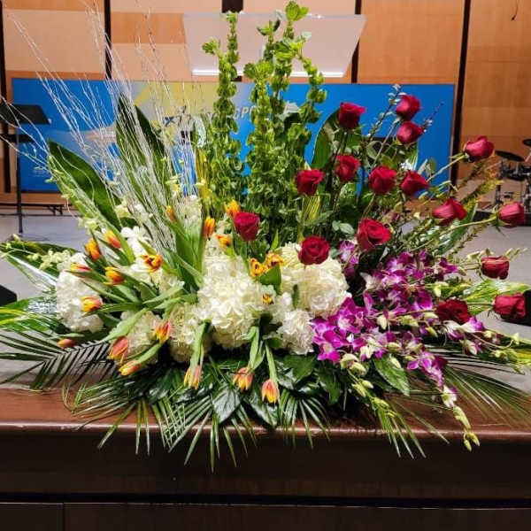Large altar-style arrangement with red roses, white hydrangeas, orchids, tulips, and tall green spikes.