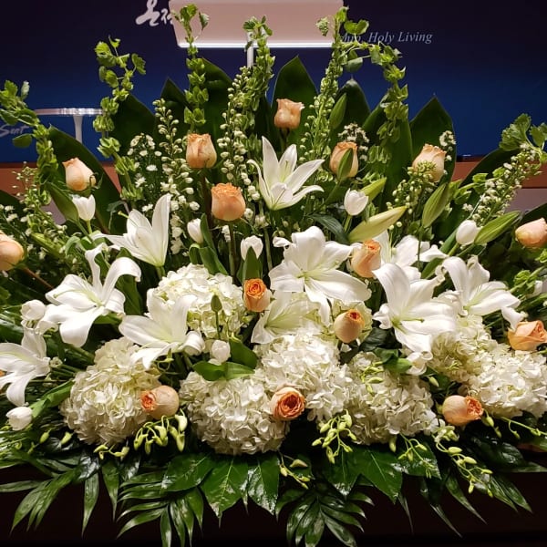 Low, wide arrangement of white lilies, hydrangeas, and peach roses on a stage