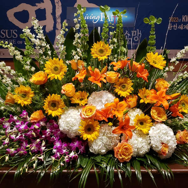 Large altar arrangement of orange lilies, yellow blooms, white hydrangeas, and purple orchids